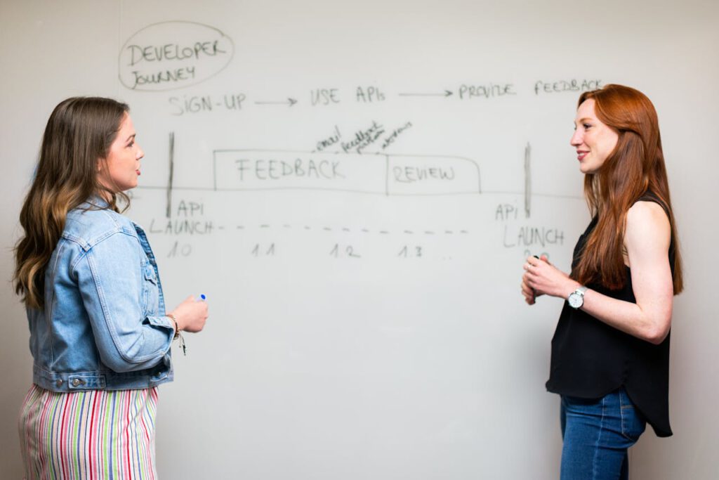 Two women engaging in a discussion about API development processes at a whiteboard.